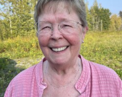 Director Bunty Althaus is a Retired Business owner for Tatogga Resort. She loves her sewing machine, family , friends, Terrace, Victoria and Tatogga Lake in that order. She is known for her attention to detail and her amazing quilts and we count ourselves very lucky to have her. Woman wearing an open pink blouse with a black underneath. She is smiling. Bacground is a field with deciduous trees against a blue sky.